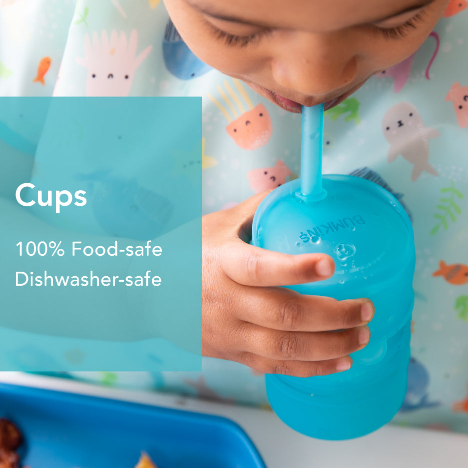 Child drinking from a blue cup with a straw, wearing a bib decorated with colorful animals. Text on the image highlights: Cups, 100% Food-safe, Dishwasher-safe. A blue tray is partially visible.