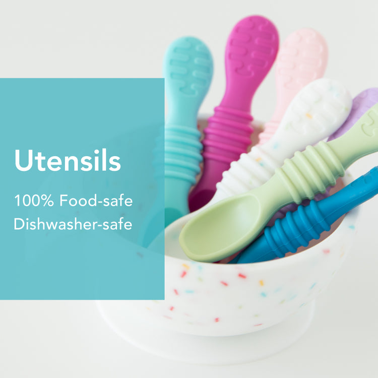 A bowl filled with colorful baby utensils, including pink, blue, and purple spoons, with a text overlay stating, Utensils, 100% Food-safe, Dishwasher-safe. The bowl has a confetti-like pattern.