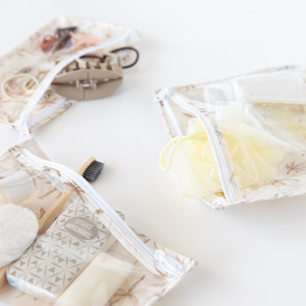 Bumkins Clear Travel Bag 3 Pack: Palm Daze holds toiletries like a toothbrush, soap, sponge, and hair ties on a white background.