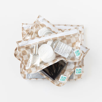 Bumkins Clear Travel Bag 3 Pack: Sand Check holds travel essentials like nail polish, cotton pads, and a small bottle on a white background.