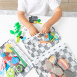 A child reaches for toys in bags from Bumkins The Outfit Organizer Essential 5-Piece Set: Charcoal Check on a white table.