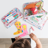 A child colors at a white table near 3 bags from Bumkins The Playdate Planner Deluxe 5-Piece Set: Boots with toys, books, & markers.