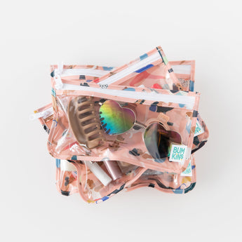 The Bumkins Clear Travel Bag 3 Pack: Yoga Pals are stacked on a white background with sunglasses, a hair clip, and lipsticks inside.