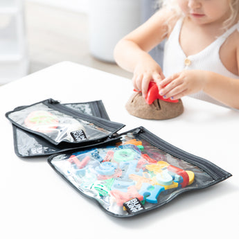 A child plays with clay; Bumkins Clear Travel Bag 3 Pack: Rich Black hold colorful alphabet cutters in the foreground.