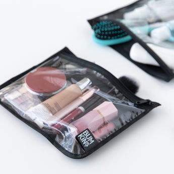Bumkins Wet Bag + Clear Travel Bag 3 Pack Set in Rich Black holds makeup, with brushes and bottles in another reusable bag behind.