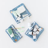 Roamio by Bumkins Clear Travel Bag 3 Pack: Crushed Denim holds toiletries and coffee pods on a white background.