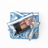 Roamio by Bumkins Clear Travel Bag 3 Pack: Crushed Denim is stacked on a white background with makeup items inside.