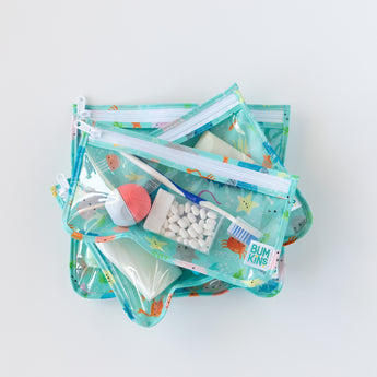 Bumkins Clear Travel Bag 3-Pack: Ocean Life, TSA compliant and reusable, filled with toiletries on a white background.