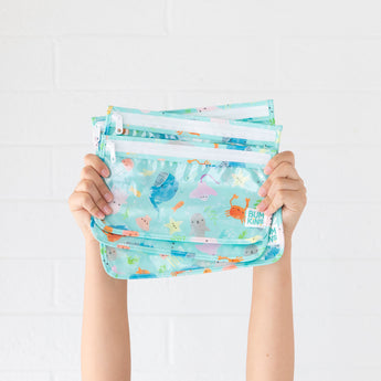 A child holds Bumkins Clear Travel Bag 3-Pack: Ocean Life—reusable, TSA-compliant bags with sea animal designs.