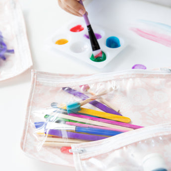 Close-up of bags from Bumkins The Chaos Coordinator Essential 4-Piece Set: Lace with art supplies next to a child's hand painting.