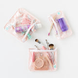 Bumkins Clear Travel Bag 3-Pack: Lace is neatly arranged on a white background with makeup, toiletries, and hair accessories inside.