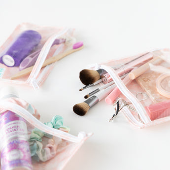 Close-up of Bumkins Clear Travel Bag 3-Pack: Lace on a white background with toiletries, makeup, and hair accessories inside.