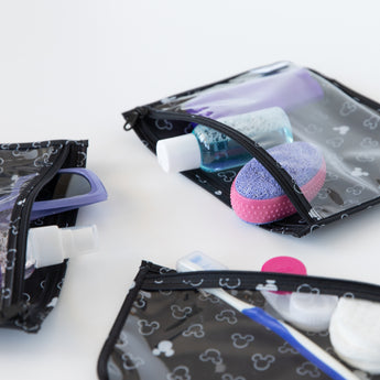 Close-up of Bumkins Clear Travel Bag 3-Pack: Mickey Mouse Icon Black + White filled with toiletries on a white background.