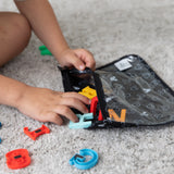 Close-up of a child reaching for letter-shaped magnets from a Bumkins Clear Travel Bag 3-Pack: Mickey Mouse Icon Black + White.