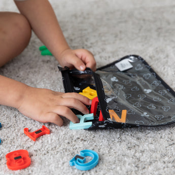 Close-up of a child reaching for letter-shaped magnets from a Bumkins Clear Travel Bag 3-Pack: Mickey Mouse Icon Black + White.