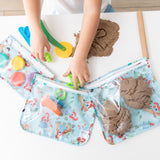 A child plays with kinetic sand and tools among Bumkins Clear Travel Bag 3 Pack: Disney Princess Ariel on a white table.