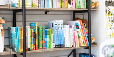 A bookshelf filled with various colorful childrens books, toys, and plush animals. The books are stacked neatly on wooden shelves. Vibrant shades of blue, green, yellow, and pink are visible among the book covers.