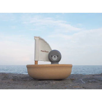 PlanToys Sailing Boat, Seal with PlanWood sail rests on rocks against a calm ocean and cloudy sky.