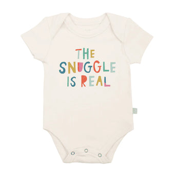 Finn and Emmas Organic Bodysuit, Snuggle Is Real, is cream-colored with colorful text: THE SNUGGLE IS REAL on the front.