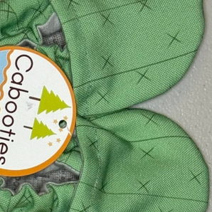Green Cabooties Cactus Spines baby bootie with rubber soles, featuring small tree illustrations for added grip.