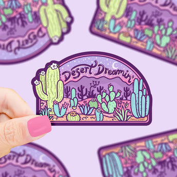 A hand holds a Turtle Soups Desert Dreaming durable waterproof vinyl sticker, featuring cacti and a desert scene under a starry sky.