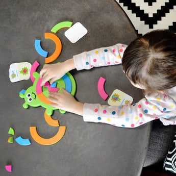 A child enjoys the Bugzzle Game by Fat Brain Toy Co, placing colorful pieces on a green turtle, with matching symbol cards scattered around.