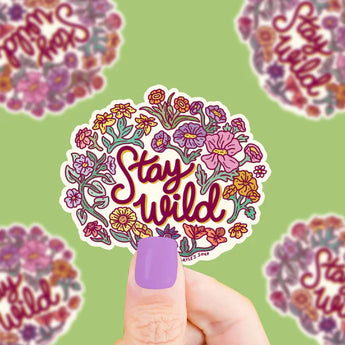 Hand holding Turtle Soups Stay Wild durable vinyl sticker featuring floral patterns on a green background.
