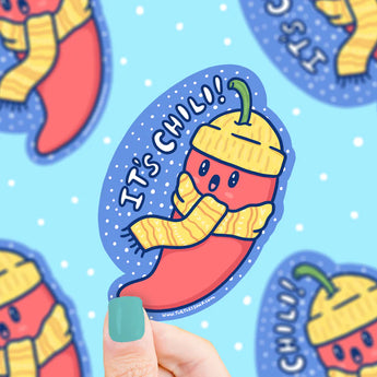 A Its Chili Pepper Cold Turtle Soup sticker shows a chili in a hat and scarf on blue, held by teal-nailed hand. Durable, waterproof vinyl!.