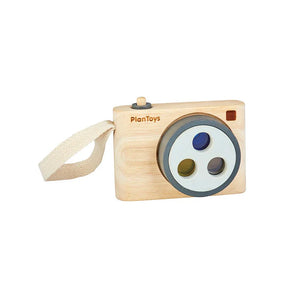 Colored Snap Camera: tan wooden camera toy with fabric strap and gray details; PlanToys logo on front.