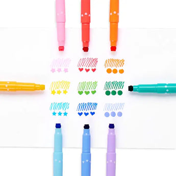 Confetti Stamp Markers by OOLY form a colorful circle, crafting hearts, stars, waves, and dots on white paper.
