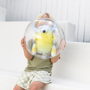 Child sits on a white bench, holding a Sunnylife 3D Inflatable Beach Ball featuring Monty the Monster, partly covering their face.