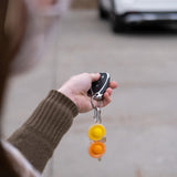 Person with car key and a clear Simpl Dimpl keychain from Fat Brain Toy Co, pointing at a parked car.