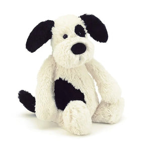 The Jellycat Bashful Black & Cream Puppy plush has black ears, a patch over one eye, and a side spot, all on a white base.
