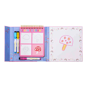 Open the Learn to Draw, Rainbow Fairy kit by Floss and Rock with a mushroom sketchbook, markers, and drawing steps; finished art on right.