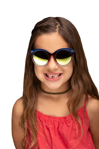 A girl with long brown hair wearing DC Wonder Woman Arkaid Sunglasses by Sunstaches, a black choker, and a red top smiles toothlessly.