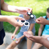 People exchanging Fat Brain Toy Cos Simpl Dimpl, Black and White outdoors, while others enjoy tactile fun on the grass in the background.