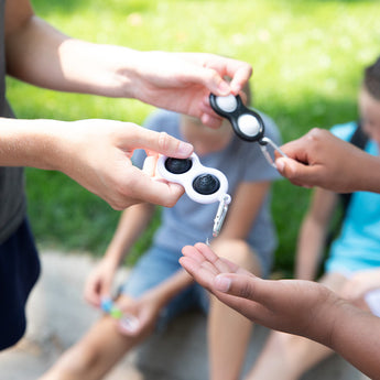 People exchanging Fat Brain Toy Cos Simpl Dimpl, Black and White outdoors, while others enjoy tactile fun on the grass in the background.