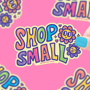 The Turtle Soup Shop Small vinyl sticker features cheerful flowers on pink, is durable, waterproof, and held by blue-manicured nails.