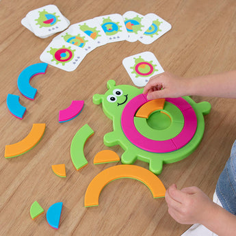 A childs hands tackle the Bugzzle Game by Fat Brain Toy Co, with vibrant puzzle and matching cards spread on the table.