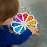 A child exercises fine motor skills with Fat Brains Dimpl Digits, a flower-shaped pop toy with colored silicone bubbles.