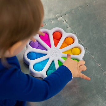 A child exercises fine motor skills with Fat Brains Dimpl Digits, a flower-shaped pop toy with colored silicone bubbles.