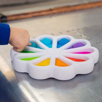 A child presses the silicone bubbles on a Dimpl Digits toy by Fat Brain Toy Co, enhancing fine motor skills on a metallic surface.