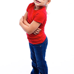 A child in a red shirt and jeans confidently poses with arms crossed, wearing Sunstaches Lil Characters Sunglasses, Wonder Woman.