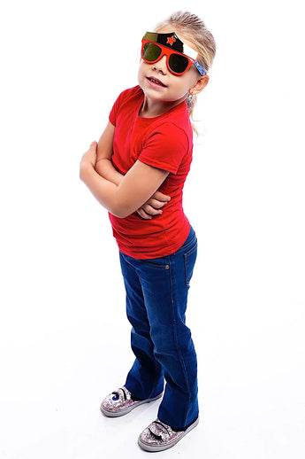 A child in a red shirt and jeans confidently poses with arms crossed, wearing Sunstaches Lil Characters Sunglasses, Wonder Woman.