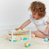 A child plays with a Janod Juratoys Wooden Xylophone on a carpet, surrounded by scattered balls, resembling a lively xylo session.