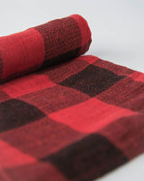 A rolled-up Cotton Swaddle in Red Plaid by Little Unicorn lies on a white background.