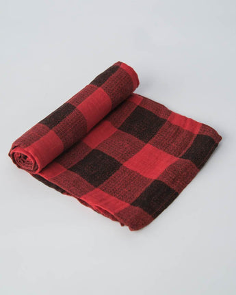 Partially rolled Little Unicorn red plaid cotton swaddle on a light gray background.