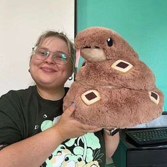 Person smiling with a large Squishable Plush Rattlesnake, its pink tongue out, in a room with teal walls.