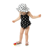 Toddler in a black daisy swimsuit and Bumkins Sun Hat: Hearts with UPF 50+ fabric, stylishly eyeing a toy ball and sun-protected.