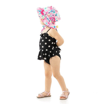 Child in black swimsuit, pink sandals, and a Bumkins Watercolor sun hat with adjustable drawstring against a white background.